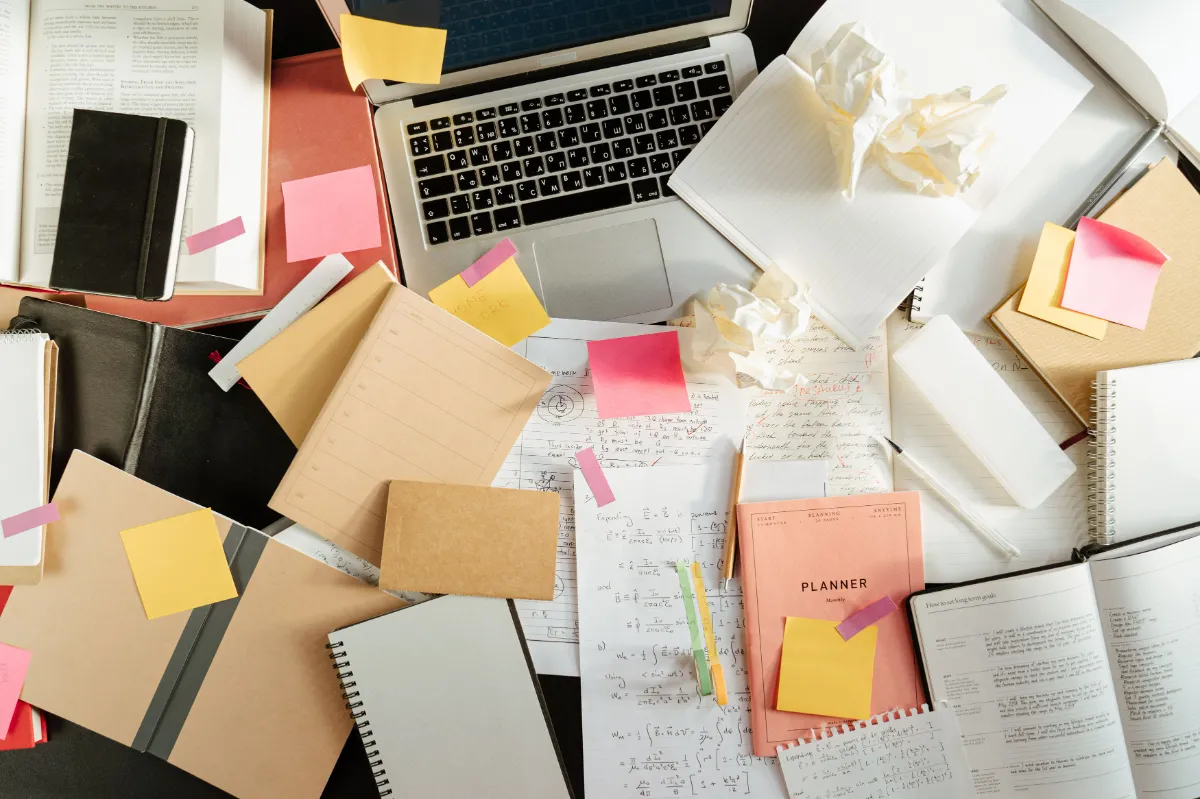 A desk covered with scattered paper notes and business cards around a laptop